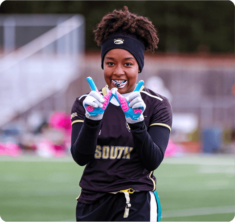 A smiling female flag football player in a black South jersey holds up two fingers and bites her mouthguard
